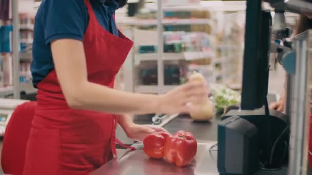 Midsectiebeelden van een onherkenbare vrouw die uitcheckt bij de grote supermarkt en kassier in rood uniform die groenten weegt. - Video