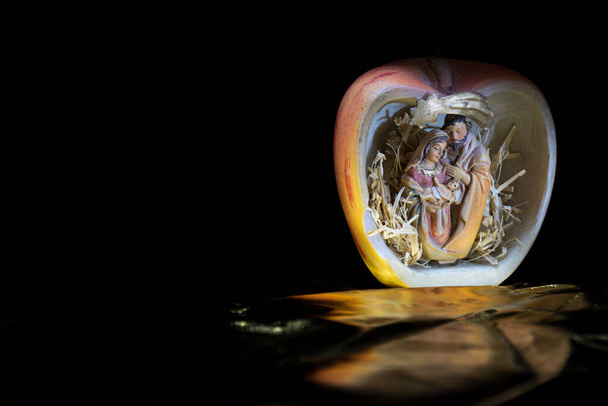 Belén en la manzana. Naturaleza muerta de la sagrada estatuilla familiar representada dentro de una manzana, con un cometa y reflejos dorados. - Foto, Imagen
