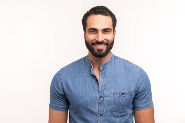 Positive handsome bearded man in blue shirt looking at camera with toothy smile, happy successful business man. Indoor studio shot isolated on white background - Foto, Imagem