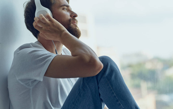 Muž sedí na parapetu a má sluchátka a poslouchá hudbu. - Fotografie, Obrázek
