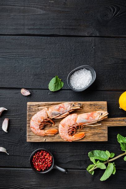Sea prawns on wooden board with ingredients on black wooden table, top view with space for text, food photo. - 写真・画像