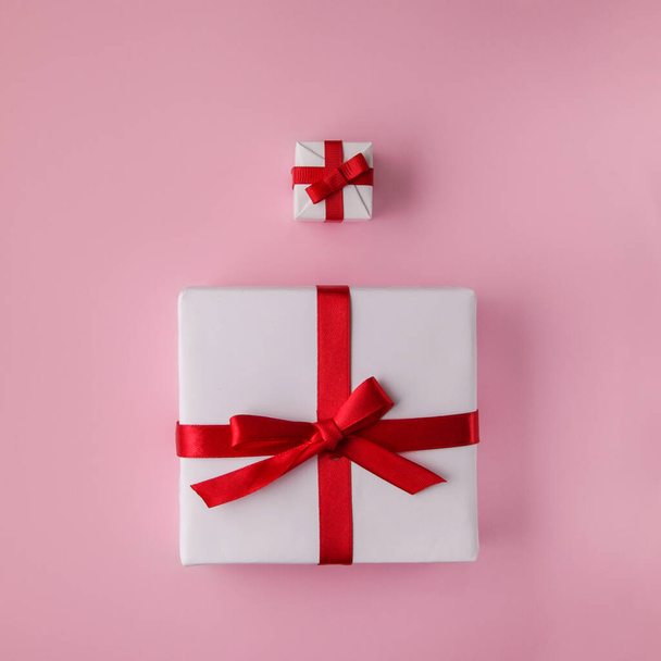 große und kleine weiße Geschenkschachtel mit rotem Band auf rosa Hintergrund. Minimalkonzept. - Foto, Bild