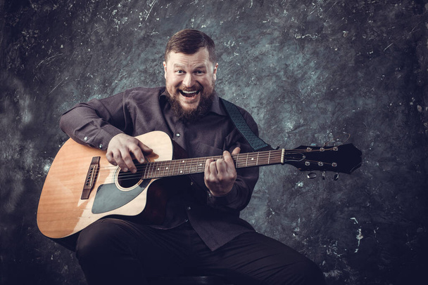 Mature musician plays acoustic guitar emotional studio portrait. - 写真・画像