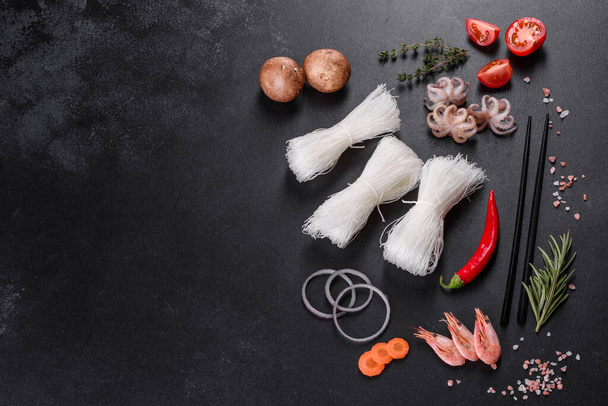Смачна рисова локшина з помідорами, червоним перцем, грибами та морепродуктами на темному бетонному фоні
 - Фото, зображення