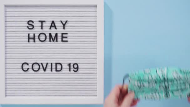 STAY HOME y COVID-19 firman en el tablero de mensajes con una mascarilla casera. - Imágenes, Vídeo