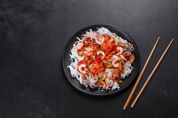 Nouilles de riz savoureuses à la tomate, au poivron rouge, aux champignons et aux fruits de mer sur un fond de béton foncé - Photo, image