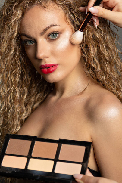 Make-up kunstenaar met professionele contouren palet en borstel in de buurt van het gezicht van de vrouw. Close-up atelierportret - Foto, afbeelding