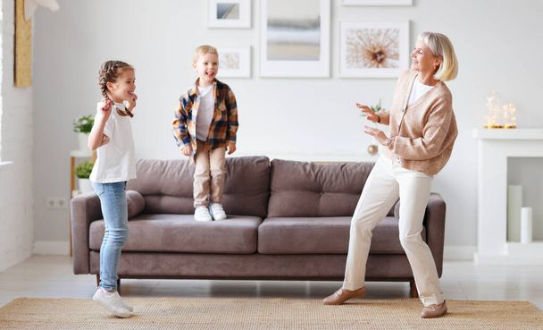 Delighted mature woman dancing with cute kids in living room while having fun and spending weekend together at hom - Fotoğraf, Görsel