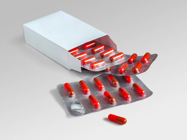Caja de cartón con blisters, que son cápsulas selladas de gelatina de color rojo, sobre un fondo gris claro - Foto, Imagen
