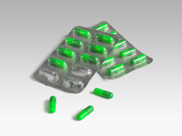 Capsule di gelatina verde in blister lucidi isolati su fondo grigio chiaro - Foto, immagini
