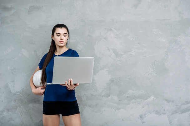 若い女の子は、ノートパソコン上でオンラインチュートリアルを見てバレーボールボールと演習を行う。スポーツコーチはオンラインレッスンを導く。オンラインワークアウトの概念。ヴィンテージカラーフィルター - 写真・画像
