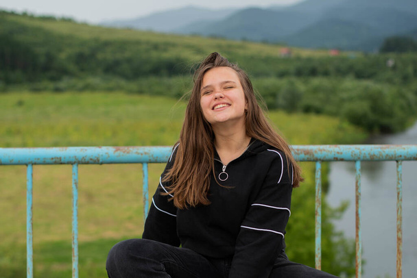 Χαρούμενα συν μέγεθος έφηβος κορίτσι φορώντας το περπάτημα κοντά στα βουνά. χαμογελαστός, χαρούμενος, θετική συγκίνηση, ευτυχία απολαμβάνουν εναλλακτικό τρόπο ζωής. Πραγματικό αφιλτράριστο άνθρωποι έννοια - Φωτογραφία, εικόνα