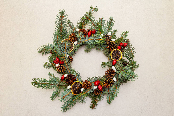 モミの木の枝、ローズヒップベリー、ドライレモンスライス、マシュマロとゼロ廃棄クリスマスリース。新年の気分、石の具体的な背景、トップビュー - 写真・画像