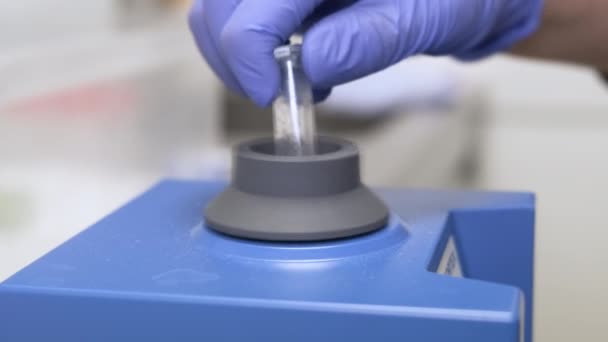 Químico en guantes de goma agitando muestras usando vórtice. Desarrollo de medicamentos y farmacéuticos - Imágenes, Vídeo