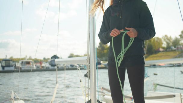 A beautiful girl athlete in sports clothes pulls a rope before traveling on a white sailing yacht on the river - Foto, Bild
