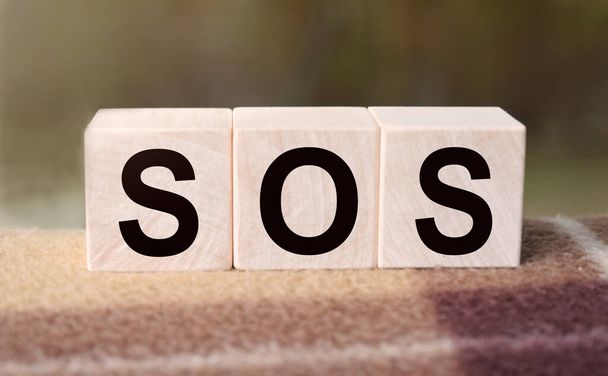 The word SOS is written on wooden cubes. Wooden cubes in the open air, overlooking the countryside. For business related design. Marketing concept. - Zdjęcie, obraz