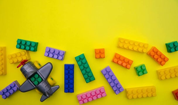 The plane is made of designer parts and cubes are scattered on a yellow background. Multi-colored construction blocks. Children's educational game. Background and texture. - 写真・画像