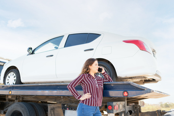 Side view of a young woman calling on the phone to ask for a ride because her car broke down on the highway and is being towed on a tow truck - Photo, Image