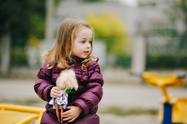 Klein meisje in paars jasje buiten in de herfst. Kind meisje met blond haar op een wandeling. Jeugd - Foto, afbeelding