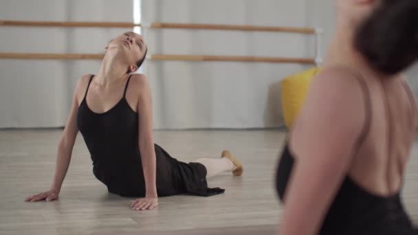 Симпатичная танцовщица растягивает шею, лежа на полу в танцевальном зале и нагибаясь сзади. Слоумоция - Кадры, видео