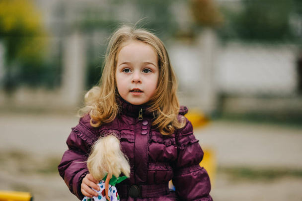 Κοριτσάκι με μωβ μπουφάν έξω το φθινόπωρο. Κοριτσάκι με ξανθά μαλλιά σε βόλτα. Παιδική ηλικία - Φωτογραφία, εικόνα