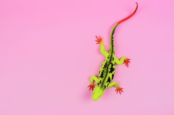 Жовта ящірка з червоними ногами на рожевому тлі крупним планом. Дитячі гумові іграшки
 - Фото, зображення