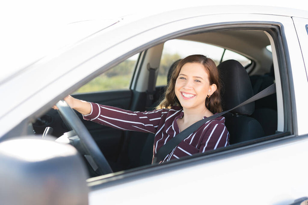 Portrait d'une jolie femme dans la vingtaine avec un visage heureux conduisant sur l'autoroute avec sa ceinture de sécurité sur - Photo, image