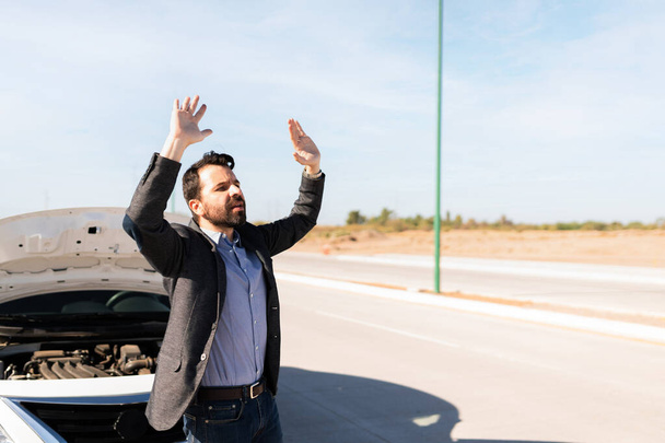 Hispanic man in his 30s waving to passing drivers for help and road assistance because his car battery is flat - Photo, Image