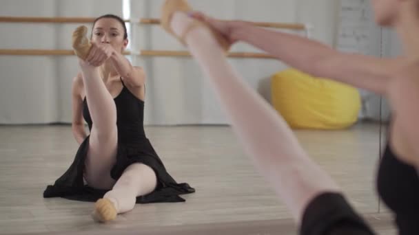Dans salonunda dans pistinde dans eden tatlı balerin kız yerde aynanın önünde bacak esneme egzersizi yapıyor. - Video, Çekim