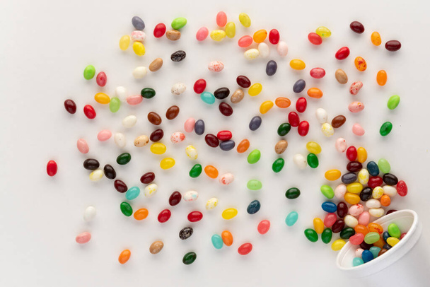  Jelly fazole vytékající z bílého pěnového kelímku na bílém pozadí, slavnostní a barevné složení se sladkostmi, nad hlavou střela s dynamickým pocitem  - Fotografie, Obrázek