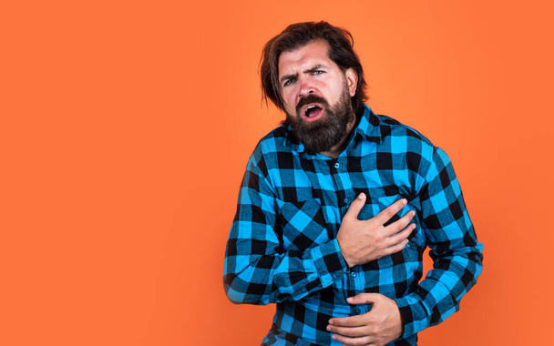 man has heartache on orange background. brutal bearded hipster feel pain. mature guy with moustache on face. expressing human emotions. suffering man in checkered shirt. copy space - Photo, image