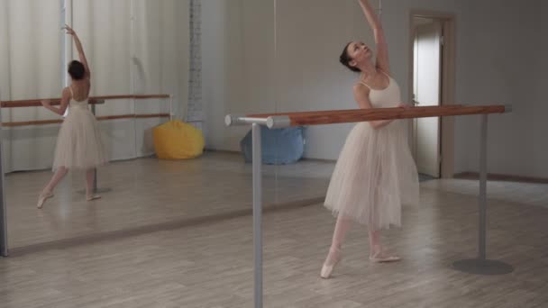 Изящная балерина девушка в танцевальном зале делает красивые изгибы перед зеркалом - Кадры, видео