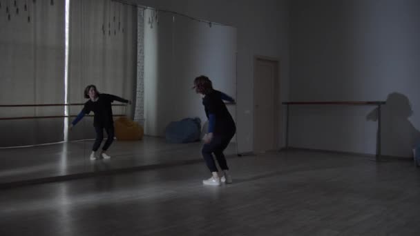 Широкий знімок танцювальної студії, де молода дівчина танцює перед дзеркалом в різних напрямках сучасного танцю
. - Кадри, відео