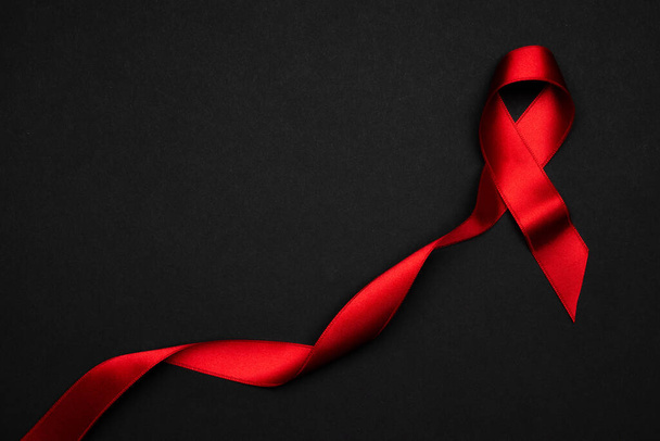 Rubans anti-cancer. Ruban rouge symbole dans la journée du monde hiv sur fond noir. Aides à la sensibilisation et cancer. Pose plate, vue du dessus, espace de copie. - Photo, image