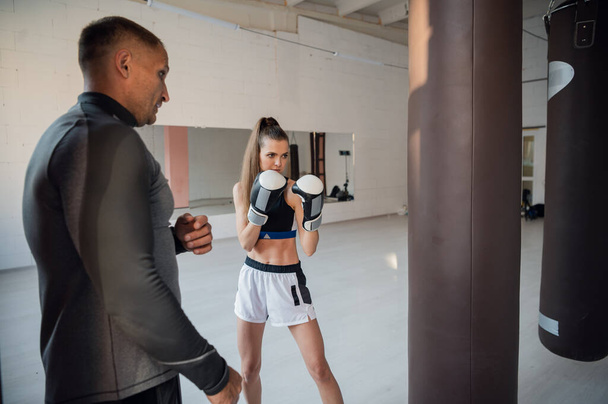Father is preparing his young daughter for mixed martial arts competitions. The girl hits a punching bag - Fotografie, Obrázek