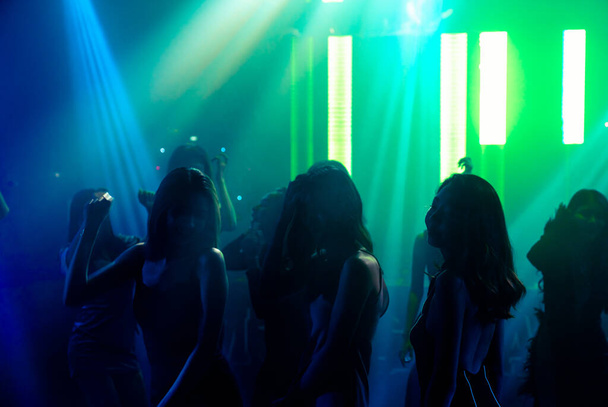 Silhouet beeld van mensen dansen in disco nachtclub op muziek van DJ op het podium - Foto, afbeelding