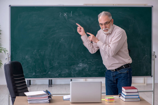 Egy öreg férfi tanár ül az osztályteremben. - Fotó, kép