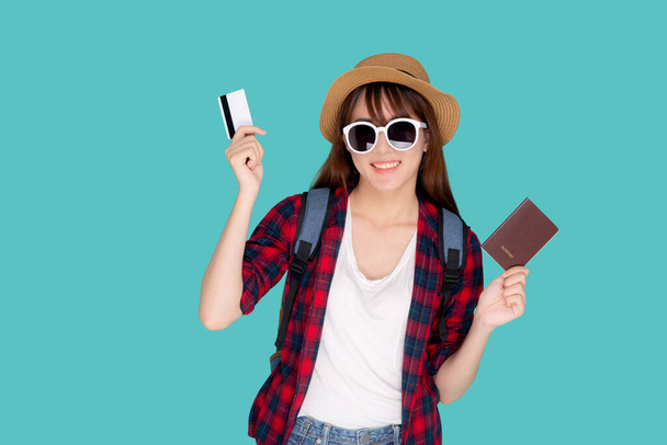 Güzel genç Asyalı kadın şapka takıyor ve güneş gözlüğü takıyor. Yaz seyahatinde kredi kartı ve pasaport gösteriyor. Mavi arka planda izole edilmiş.. - Fotoğraf, Görsel