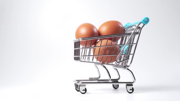 Bruine kippeneieren in een mini winkelwagentje in een supermarkt op een witte achtergrond. Shopping miniatuur concept. Dolly neergeschoten. - Video