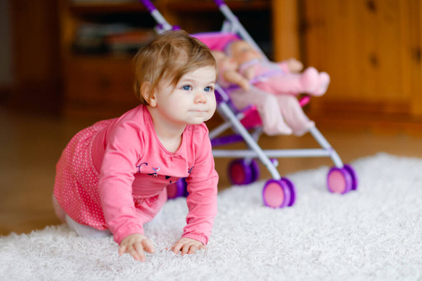 Cute adorable baby girl crawl and play with doll carriage. Beautiful toddler child with pushing stroller with toy at home. Happy kid with two dolls - Photo, Image