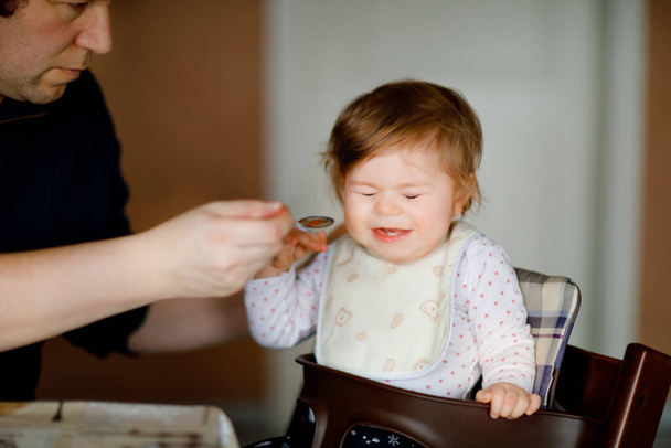 Father feeding baby girl from spoon mashed vegetables and puree. food, child, feeding and people concept -cute toddler, daughter and dad with spoon sitting in highchair and eating at home. - Photo, Image