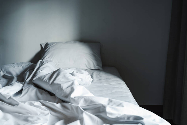 The blankets on the crumpled mattress in the empty dark bedroom - Foto, Imagen
