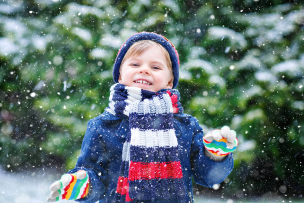 Bonito menino engraçado em roupas coloridas de moda de inverno se divertindo e brincando com a neve, ao ar livre durante a queda de neve - Foto, Imagem