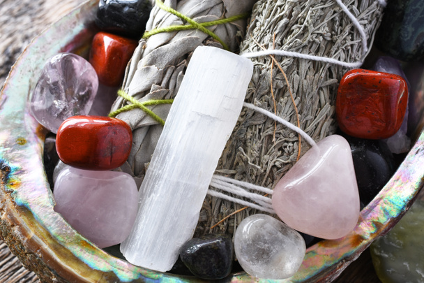 Una imagen de cerca de dos paquetes de salvia blanca con varios cristales curativos en una concha de abulón.  - Foto, imagen