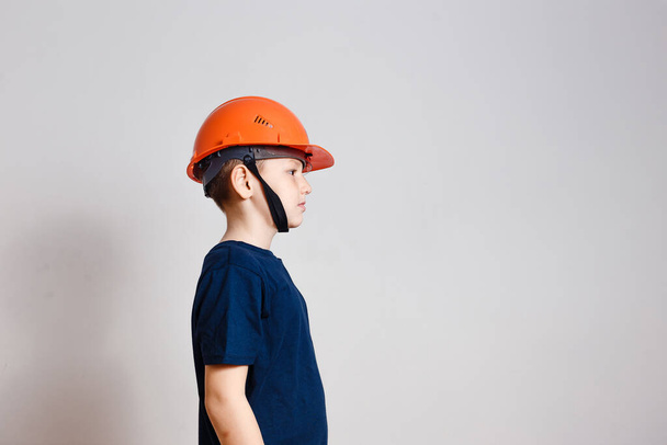 serious eight-year-old boy in orange helmet working on white background - Fotó, kép