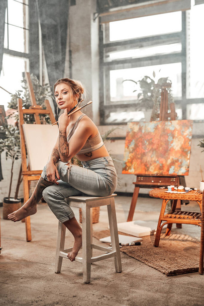 Seductive designer sitting on chair and holding paintbrushes - Photo, Image