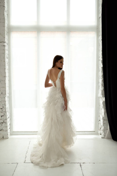 Portré egy gyönyörű menyasszony teljes növekedés a stúdióban, fehér háttérrel. A nő háttal áll, és belenéz a keretbe.. - Fotó, kép