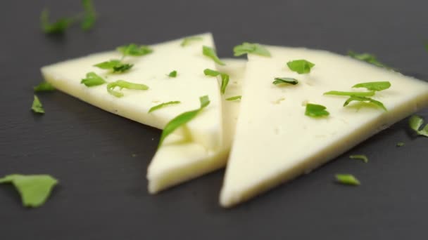 Close-up of chopped fresh parsley falls on pieces of sheep cheese. On a black stone surface. Slow motion. Dolly Shot - Footage, Video
