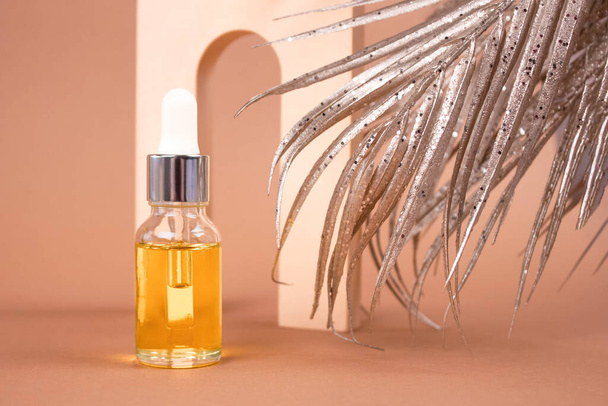 Mockup image of dropper bottle of organic cosmetics - hyaluronic acid, serum, moisturizer or facial lifting anti-aging oil. Essential oil in neutral biege still life composition with palm leaves - Photo, Image