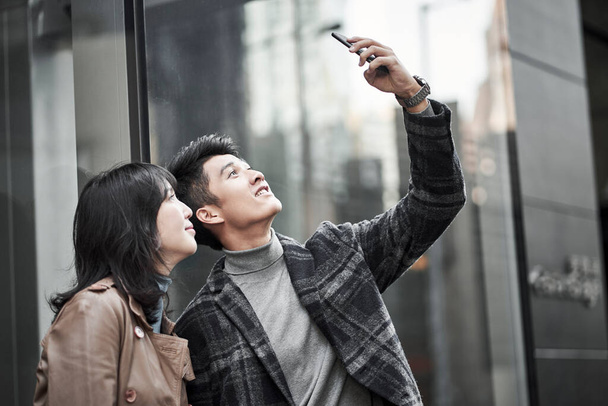 szczęśliwy młody Azji para biorąc a selfie poza a dom towarowy - Zdjęcie, obraz